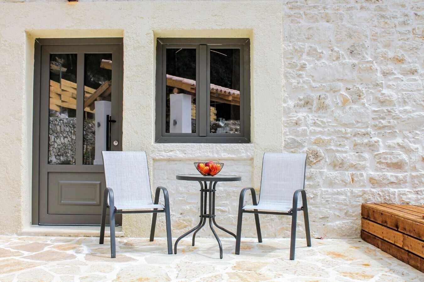 A stone building with two windows, a door, and a small table with chairs.