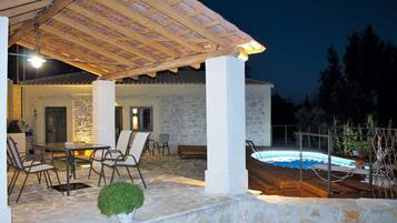 A covered outdoor area with a pool, stone flooring, and a dining setup.