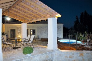 Un'area esterna coperta con piscina, pavimento in pietra e un'area pranzo.