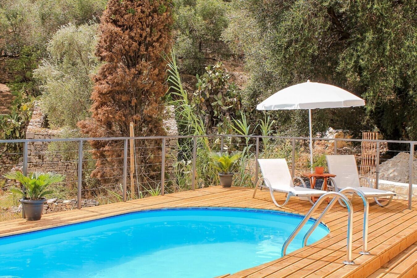 A wooden deck with a swimming pool, lounge chairs, and an umbrella.