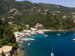Un villaggio costiero con un porto turistico, case su una collina e acque cristalline.
