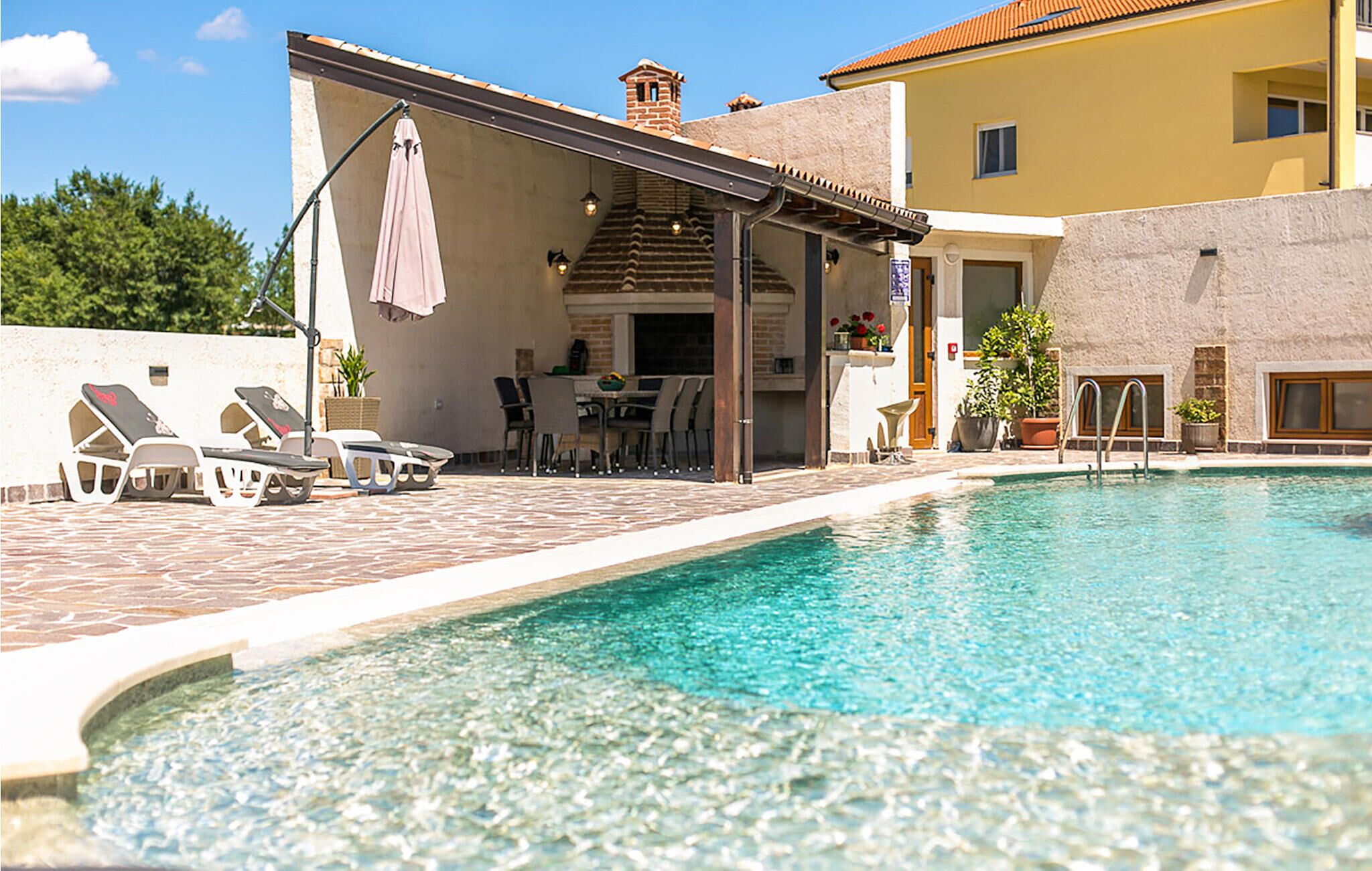 A poolside area with lounge chairs, a covered seating area, and a clear swimming pool.
