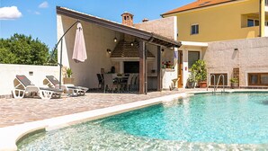 A poolside area with lounge chairs, a covered seating area, and a clear swimming pool. - Lovely apartment in Pula with swimming pool (Pula)