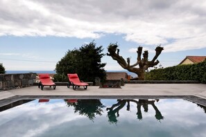 A pool with two red lounge chairs, a stone wall, and a large tree. - Holiday Home 'Ponta Da Amora' with Sea View, Wi-Fi and Air Conditioning (Ponta Garça)