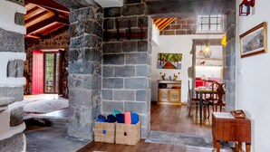 A rustic interior with stone walls, a wooden floor, a dining area with chairs and a table, and a kitchen visible through an archway. - Holiday Home 'Ponta Da Amora' with Sea View, Wi-Fi and Air Conditioning (Ponta Garça)