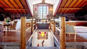 A spacious loft with a high ceiling, wooden beams, stone walls, a central staircase, and a large window. - Holiday Home 'Ponta Da Amora' with Sea View, Wi-Fi and Air Conditioning (Ponta Garça)