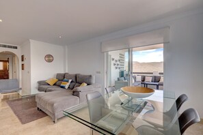 A modern living room with a glass dining table, grey sofas, and a large window with a view. - Apartment 'Casa de Mairena' with Sea & Mountain View and Wi-Fi (Elviria)