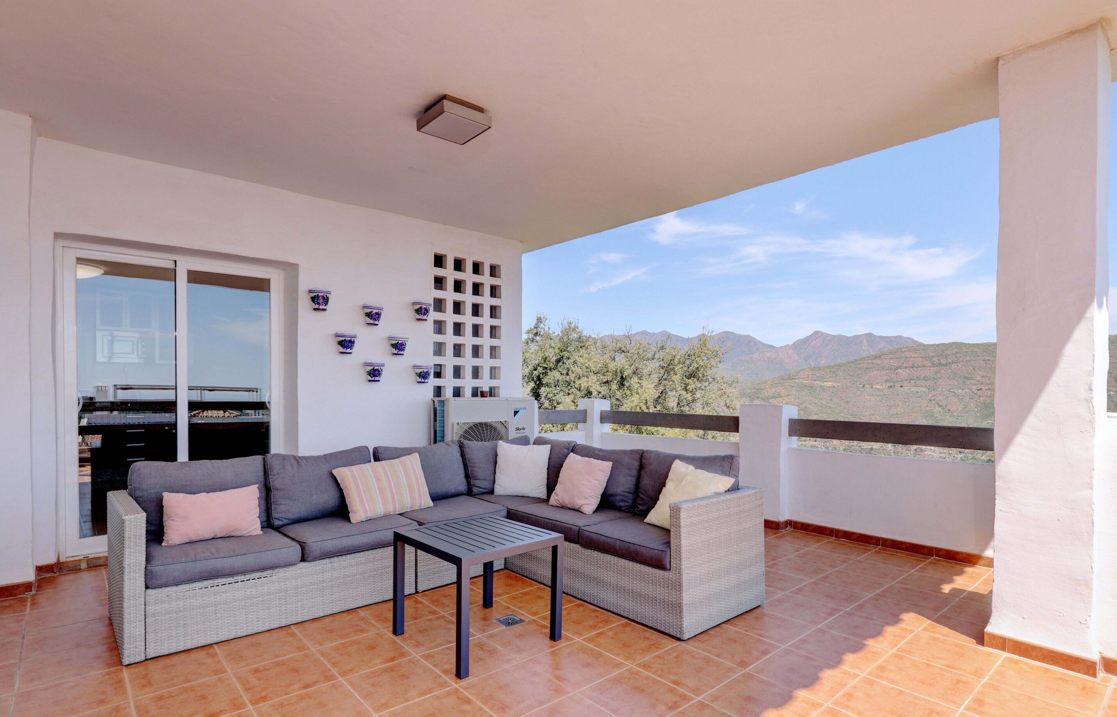 A balcony with a sofa, table, and decorative items; a sliding door; and a view of mountains.