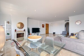 A modern living room with a glass dining table, a sofa, a flat-screen TV, and a fireplace. - Apartment 'Casa de Mairena' with Sea & Mountain View and Wi-Fi (Elviria)