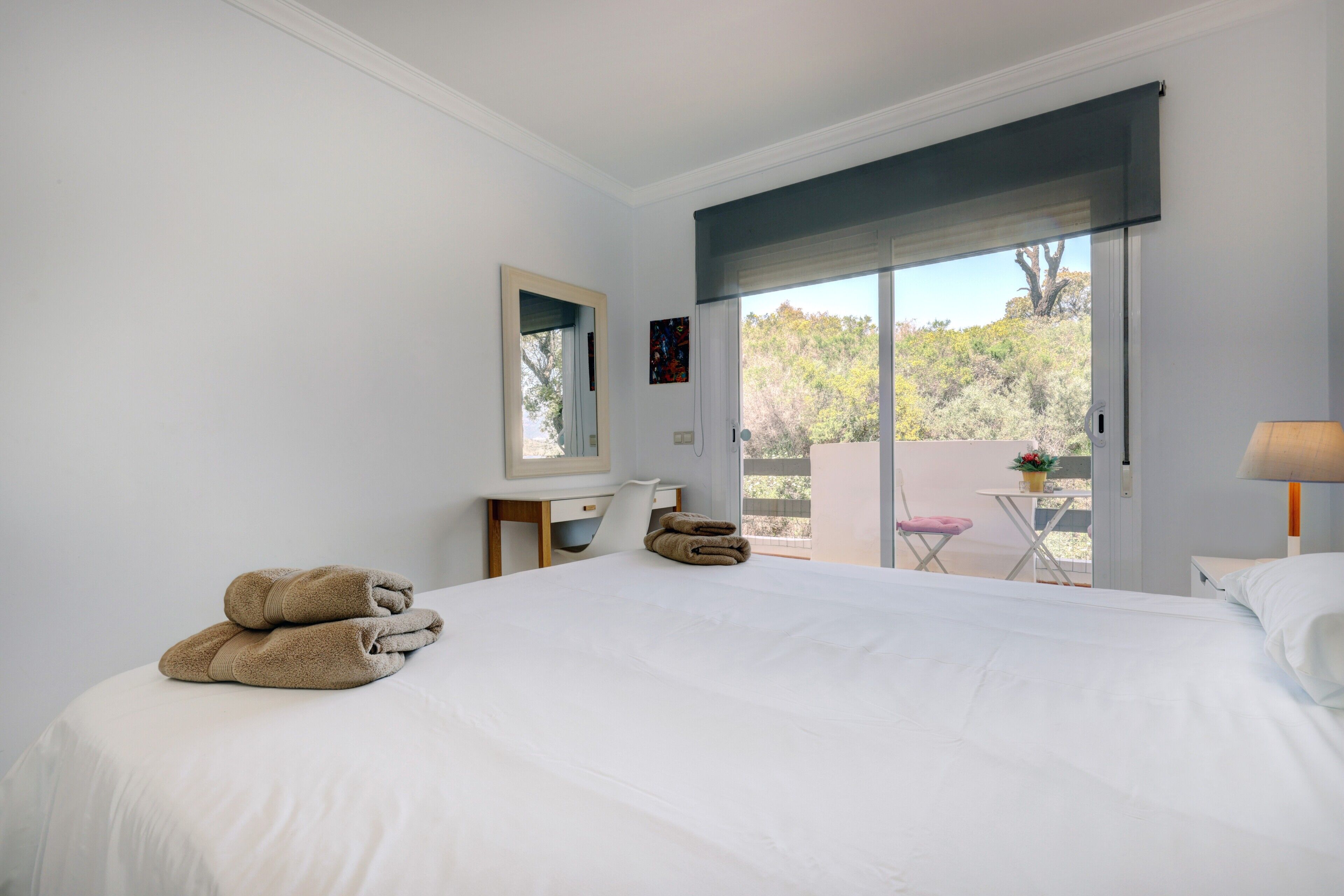 A bedroom with a bed, a desk, a chair, a window with a view, and a balcony.