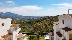 Un quartier résidentiel avec des bâtiments blancs, une piscine et une vue sur des collines lointaines.