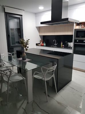 Una cocina moderna con una mesa de vidrio, sillas blancas, una isla negra y electrodomésticos de acero inoxidable.