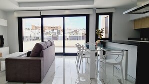 A modern living room with a sofa, a TV, and a dining area with chairs and a glass table. - Apartment 'Amanecer 7 Alicante' with Shared Pool, Wi-Fi and Air Conditioning (Orihuela)