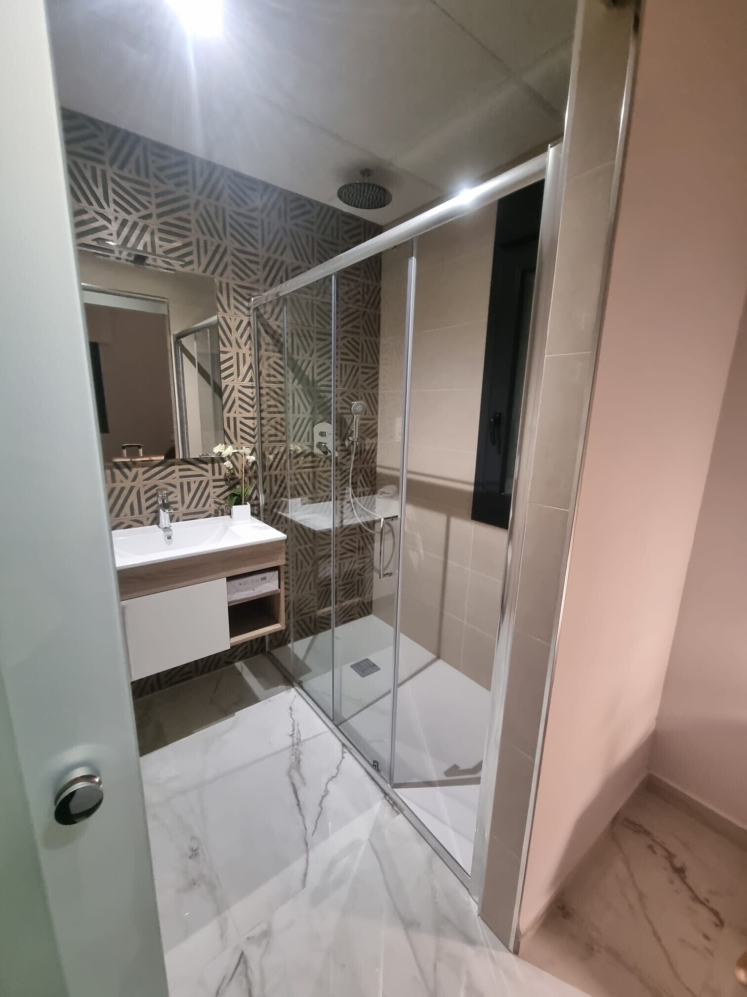 A bathroom with a glass-enclosed shower, a white sink, and patterned wall tiles.