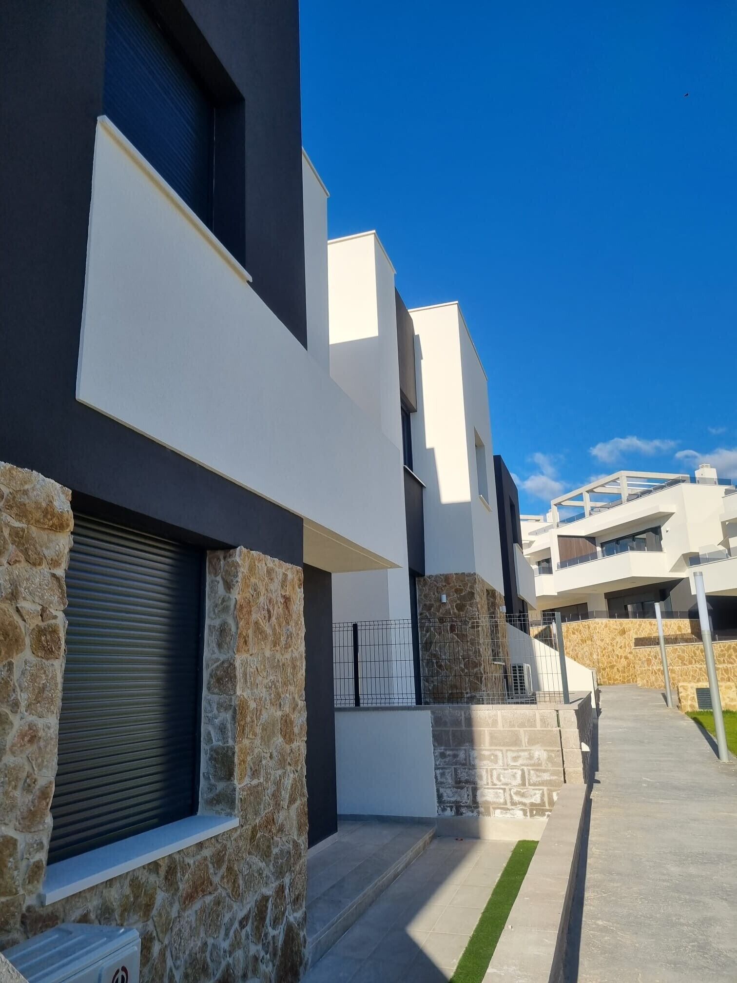 Un edificio moderno con paredes exteriores de piedra y concreto, techo plano y cielo azul despejado.