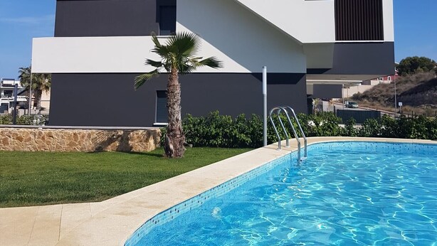 A modern building with a swimming pool, a palm tree, and a clear blue sky. - Apartment 'Amanecer 7 Alicante' with Shared Pool, Wi-Fi and Air Conditioning (Orihuela)