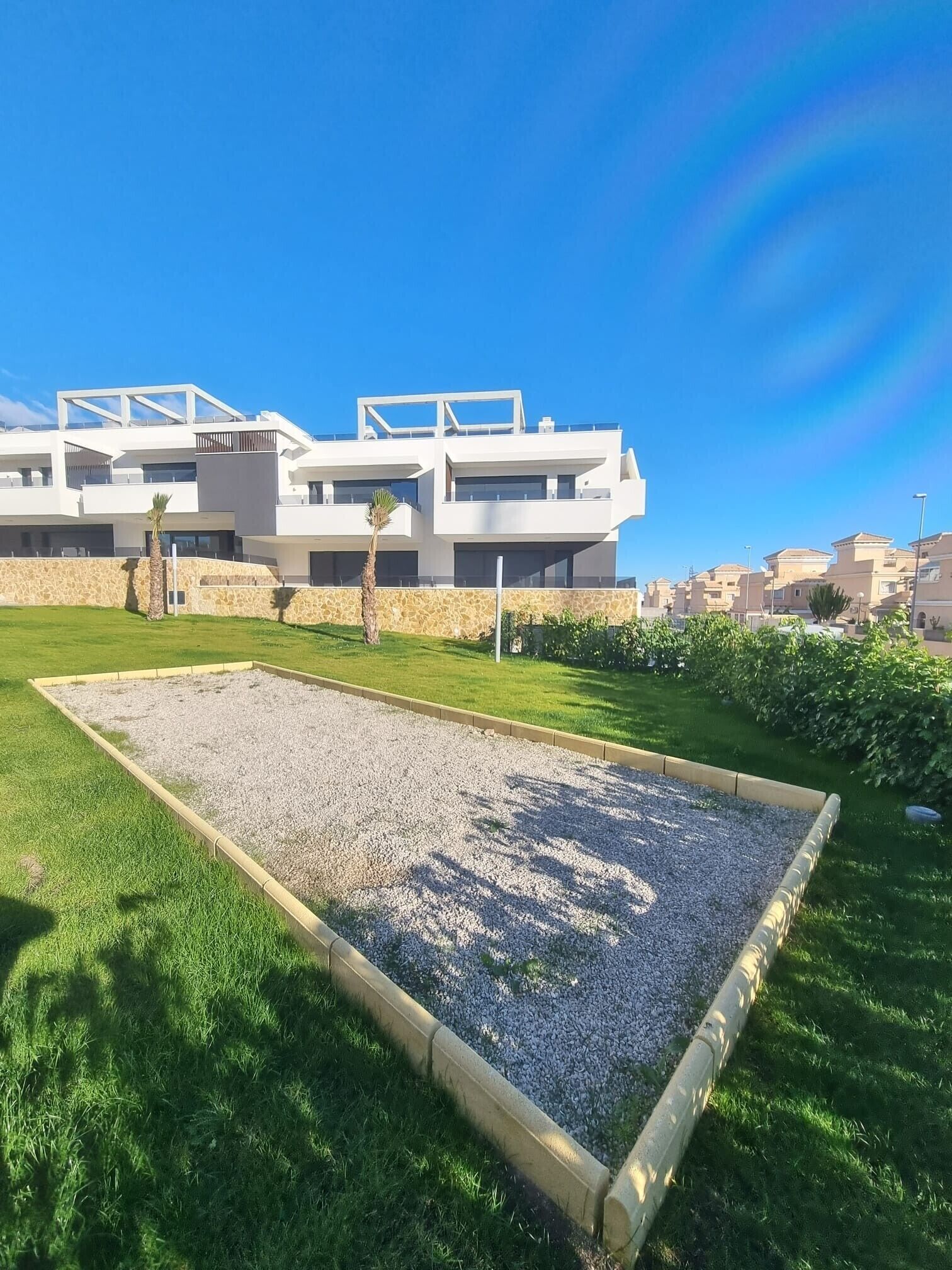Un edificio moderno con techo plano, ventanas amplias y un área pavimentada con grava y césped.
