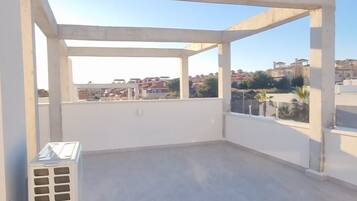 Une terrasse sur le toit, ouverte, avec une structure en béton, un climatiseur blanc et une vue sur les bâtiments environnants.