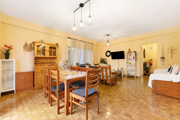 A dining area with a wooden table and chairs, a cabinet with glass doors, and a television mounted on the wall.
