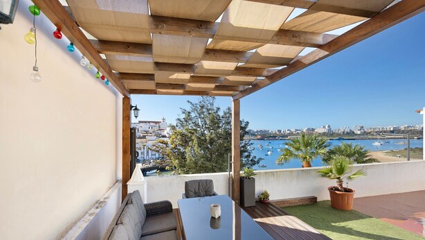 A covered outdoor seating area with a table and chairs, a view of the sea, and potted plants. - Holiday Home 'Casa Vista Rio' with Sea View, Wi-Fi and Air Conditioning (Ferragudo)