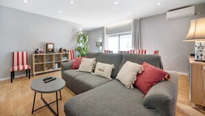 A modern living room with a grey sofa, red and white striped chair, a small round table, and a bookshelf. - Holiday Home 'Casa Vista Rio' with Sea View, Wi-Fi and Air Conditioning (Ferragudo)