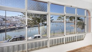 A room with large windows overlooking a marina with boats and buildings. - Holiday Home 'Casa Vista Rio' with Sea View, Wi-Fi and Air Conditioning (Ferragudo)