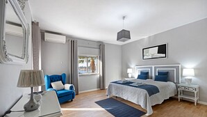 A bedroom with a bed, bedside tables, a lamp, a chair, a mirror, and a window. - Holiday Home 'Casa Vista Rio' with Sea View, Wi-Fi and Air Conditioning (Ferragudo)