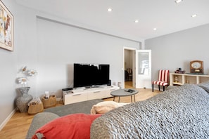 A modern living room with a flat-screen TV, a sofa, a coffee table, and a dining area with a chair and a small table.