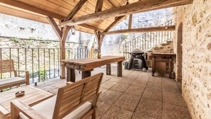 A covered outdoor patio with wooden furniture, a grill, and stone walls. - Holiday Home 'Gîte La Voisine' with Private Terrace, Wi-Fi and Air Conditioning (Venteuil)
