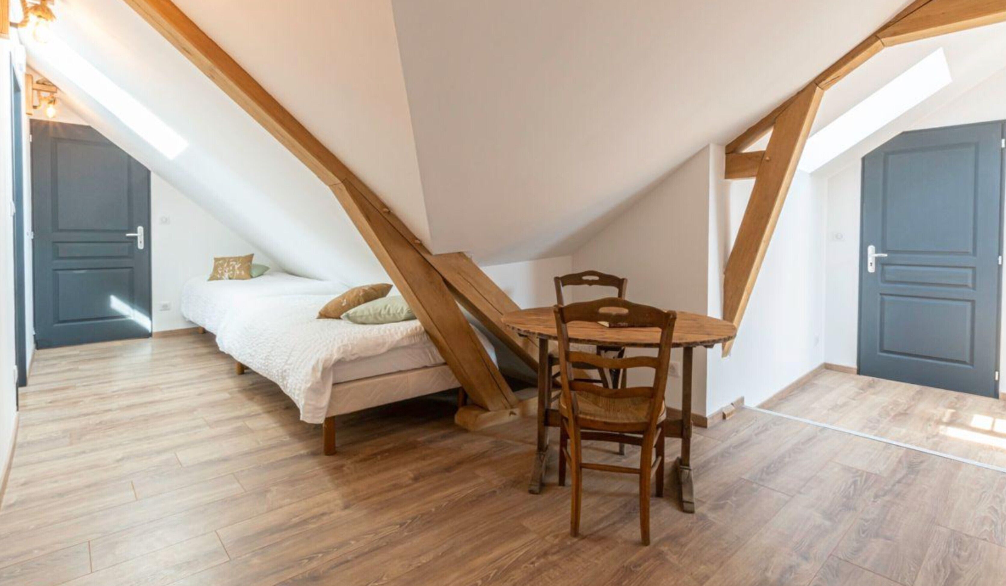 Ein Schlafzimmer im Loft-Stil mit schrägem Dach, einem Bett, einem Holztisch und einem Stuhl.