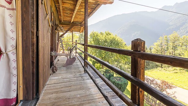 A wooden balcony with a view of mountains and greenery.