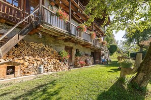 Un bâtiment rustique en bois, doté d’un balcon, d’une pile de bois de chauffage et d’une pelouse bien entretenue.