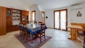 A dining area with a table, chairs, and a rug. There is a wooden cabinet with glass doors and a window. - Apartment 'Flamingo House' with Balcony, Wi-Fi and Air Conditioning (Cabras)