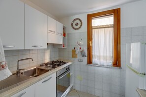 Een keuken met witte kastjes, een fornuis, een oven en een raam met gordijnen.