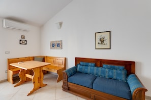 Een kamer met een houten bankje, een houten tafel, een blauwe bank en een wandairconditioner.
