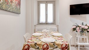 Zona pranzo con tavolo apparecchiato per quattro persone, un quadro appeso al muro e un televisore a parete.