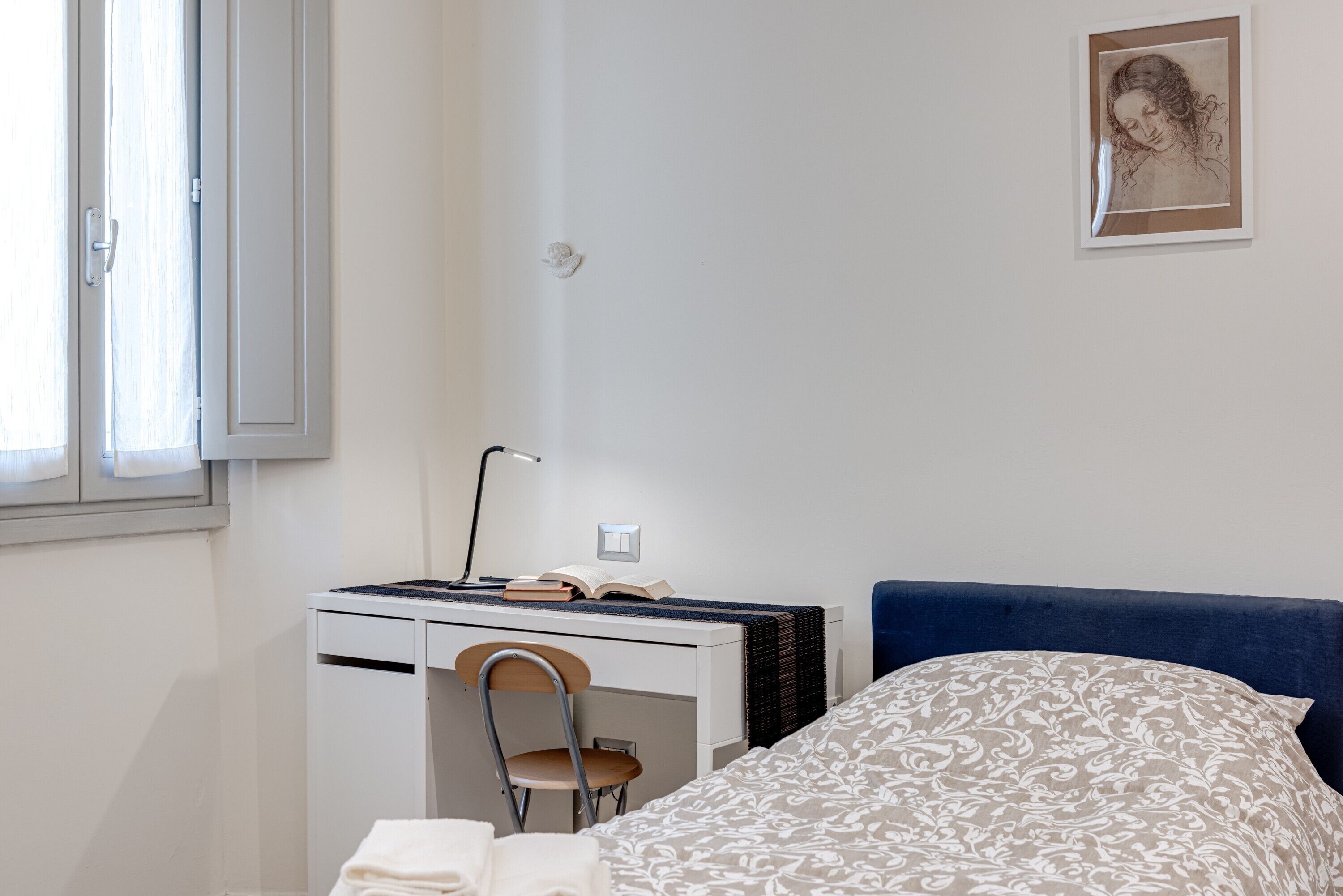Une chambre à coucher avec un lit, un bureau avec une chaise, une lampe et un tableau encadré au mur.