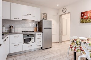 A modern kitchen with white cabinets, a stainless steel refrigerator, a microwave, and a dining area with a table and chairs.