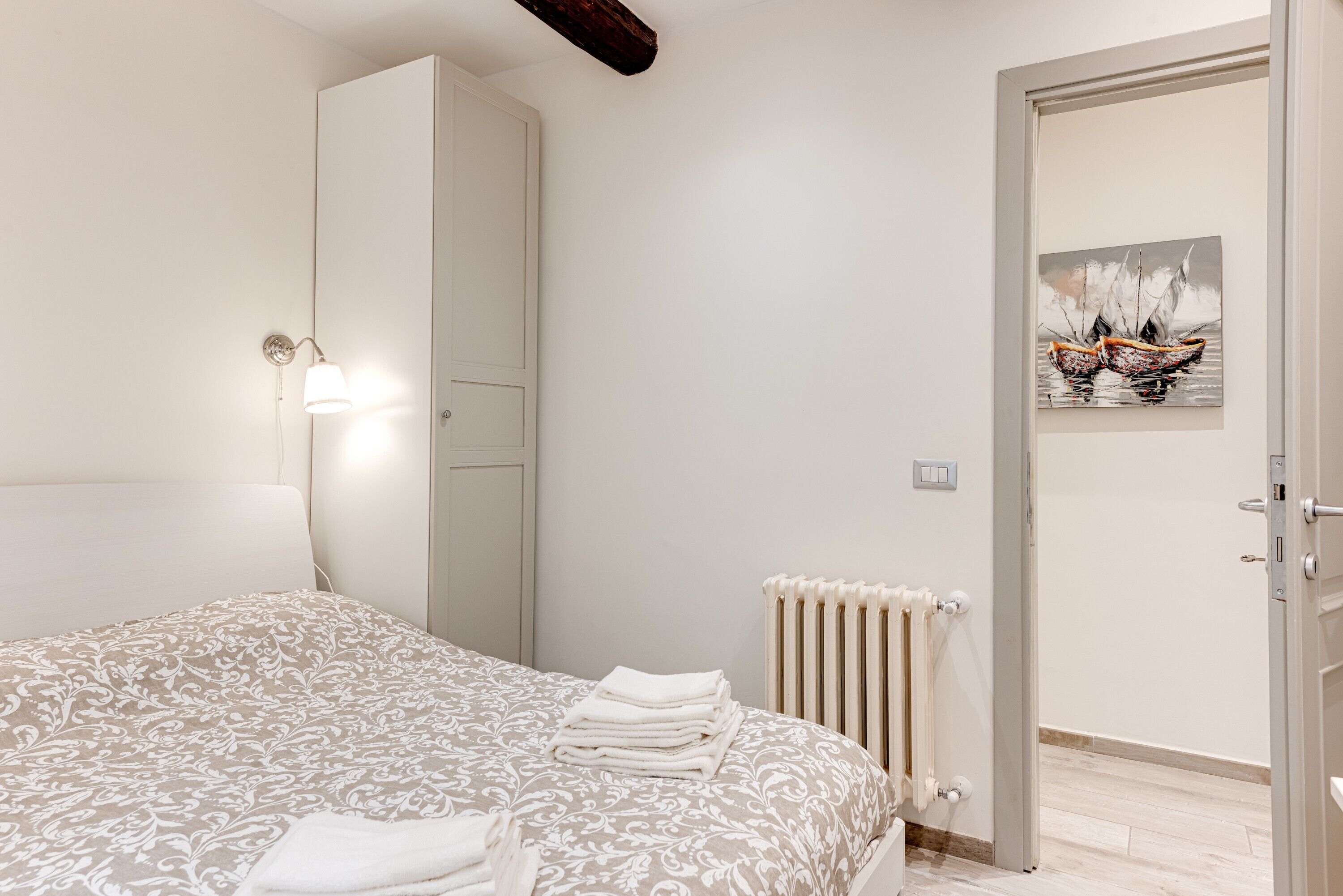 A bedroom with a bed, a wardrobe, a radiator, and a door with a painting.