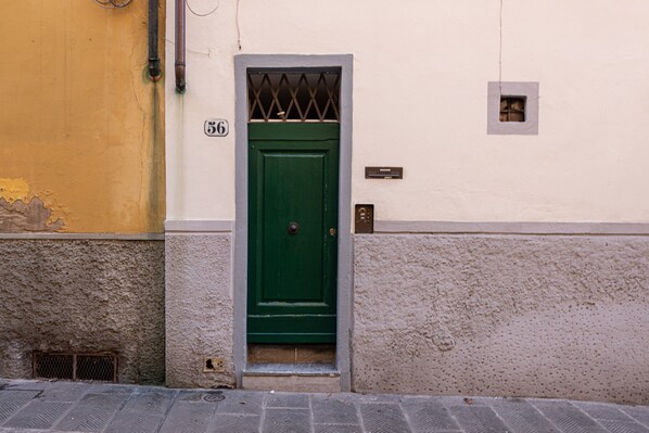 A green door with a small window above it, a number '36' on the wall, and a utility box to the right.