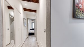 Un corridoio con un letto in fondo, travi in legno al soffitto e un quadro appeso al muro.