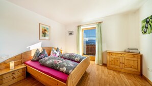Un dormitorio con cama de madera, una mesita de noche, un aparador y una ventana con cortinas.