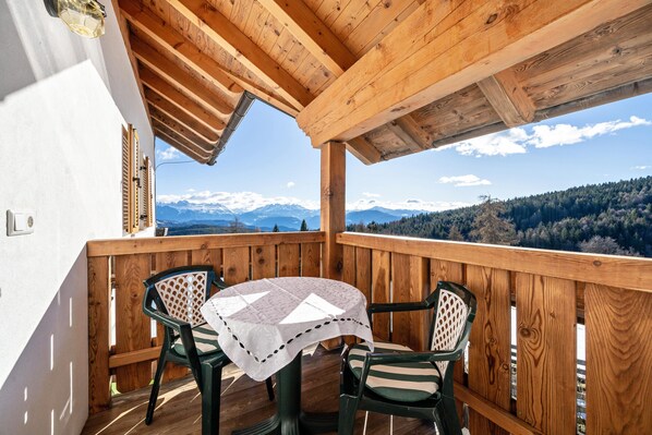 Un balcon en bois, agrémenté d’une table et de chaises, qui offre une vue sur un paysage montagneux.