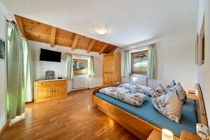 A bedroom with a wooden bed, a wooden dresser, a television, and a window with curtains.