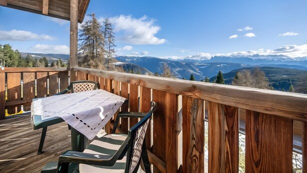Une terrasse en bois avec une table et des chaises, offrant une vue sur un paysage montagneux.