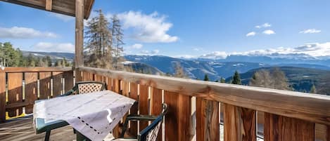 Une terrasse en bois avec une table et des chaises, offrant une vue sur un paysage montagneux.