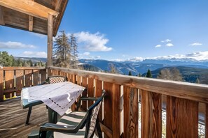 A wooden deck with a table and chairs, overlooking a mountainous landscape.
