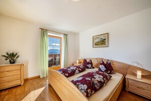 A bedroom with a wooden bed, a nightstand, a dresser, a window with a view, and a painting on the wall.