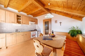 A kitchen with wooden cabinets, a dining table with a bench, a hanging plant, and a cross on the wall.