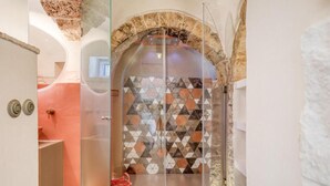 A bathroom with a glass shower enclosure, a stone archway, and a patterned tile wall. - Villa 'Borgo Trulli 1817' with Private Pool, Wi-Fi and Air Conditioning (Putignano)